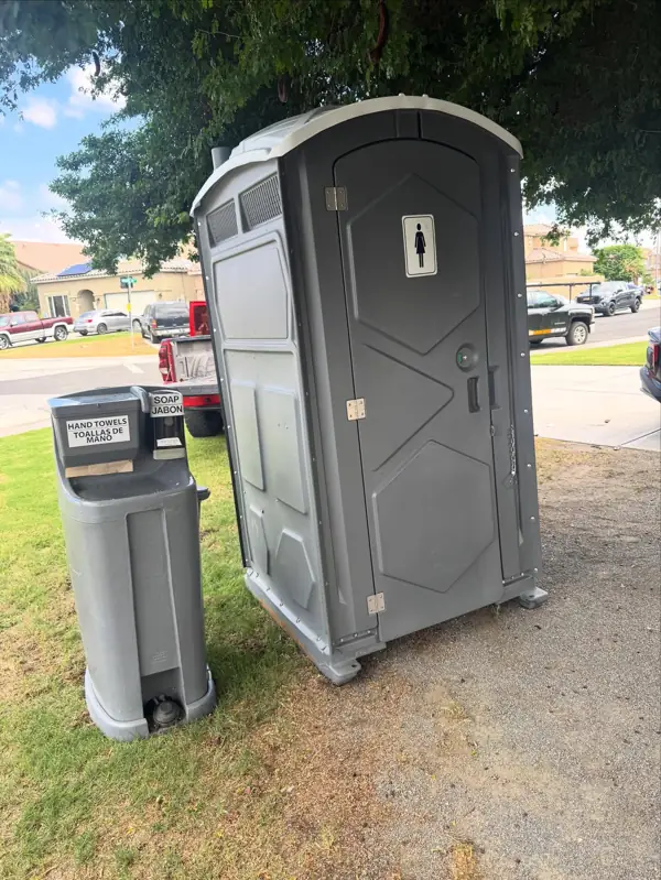 Gray portable toilet and hand wash station on a level lawn