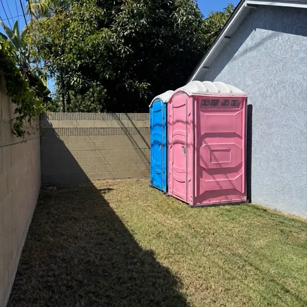 Pink and blue portable toilets in a fenced backyard