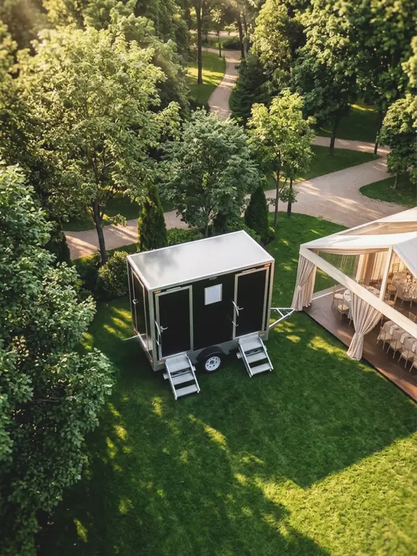 Restroom trailer set up on grass beside an event tent
