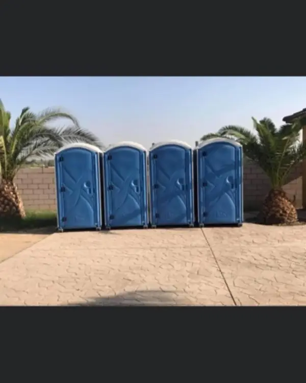 Four blue portable toilets lined up on a paved lot